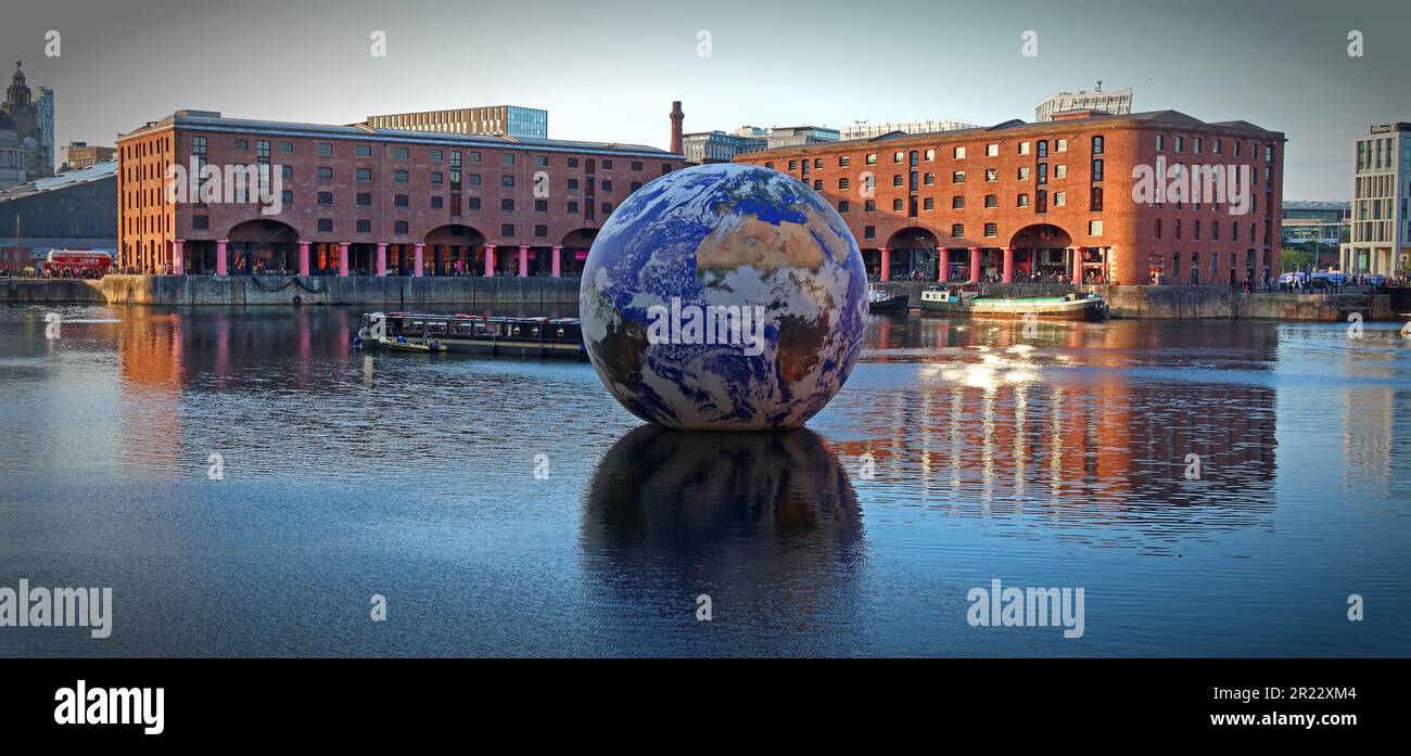 Luke Jerram Floating Earth comes to Liverpool's Royal Albert Dock, looking majestic on a sunset evening, in front of the Victorian port warehouses Stock Photo