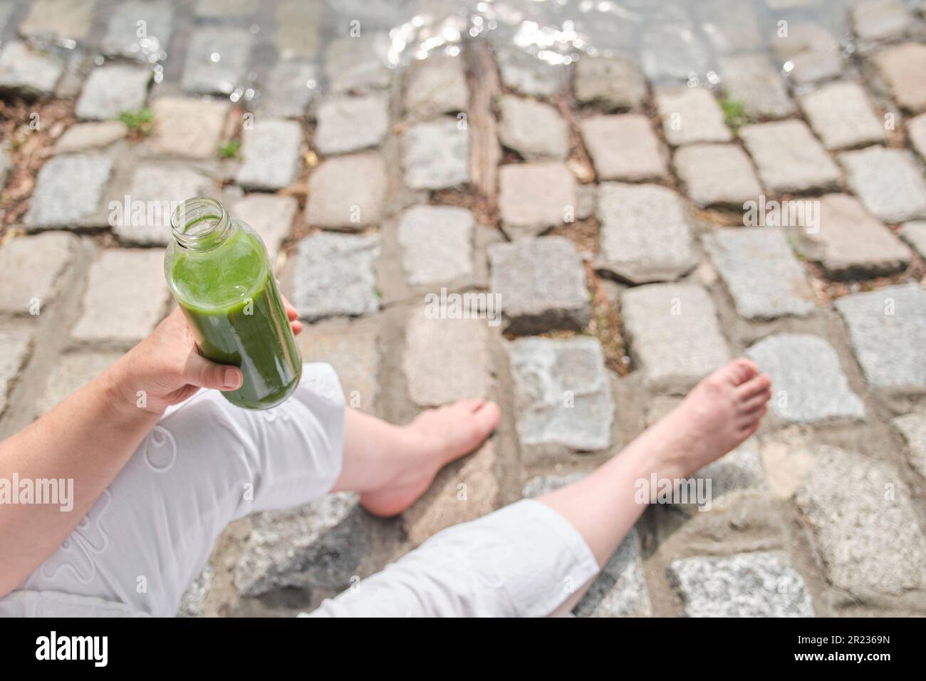 Unknown person holding a bottle of green juice outdoors. Concepts: wellness, nourishment, healthy and sustainable lifestyle. Stock Photo