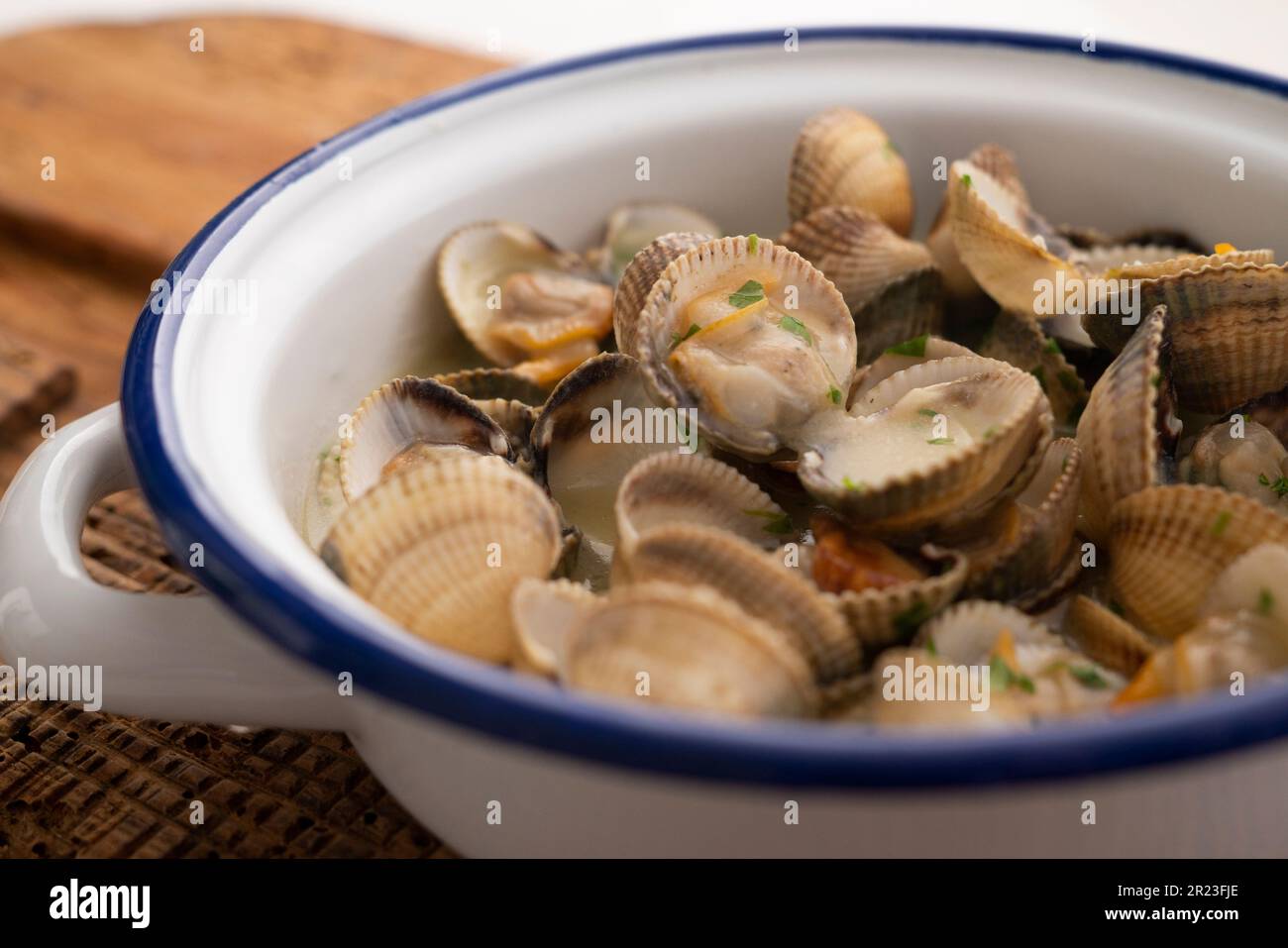 Cockles with green garlic and parsley sauce. Traditional Spanish fish tapa. Stock Photo