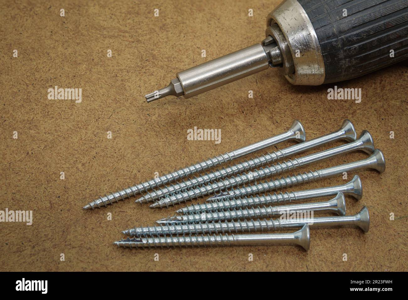 Wood screws and electric drill on top of the brown MDF board Stock