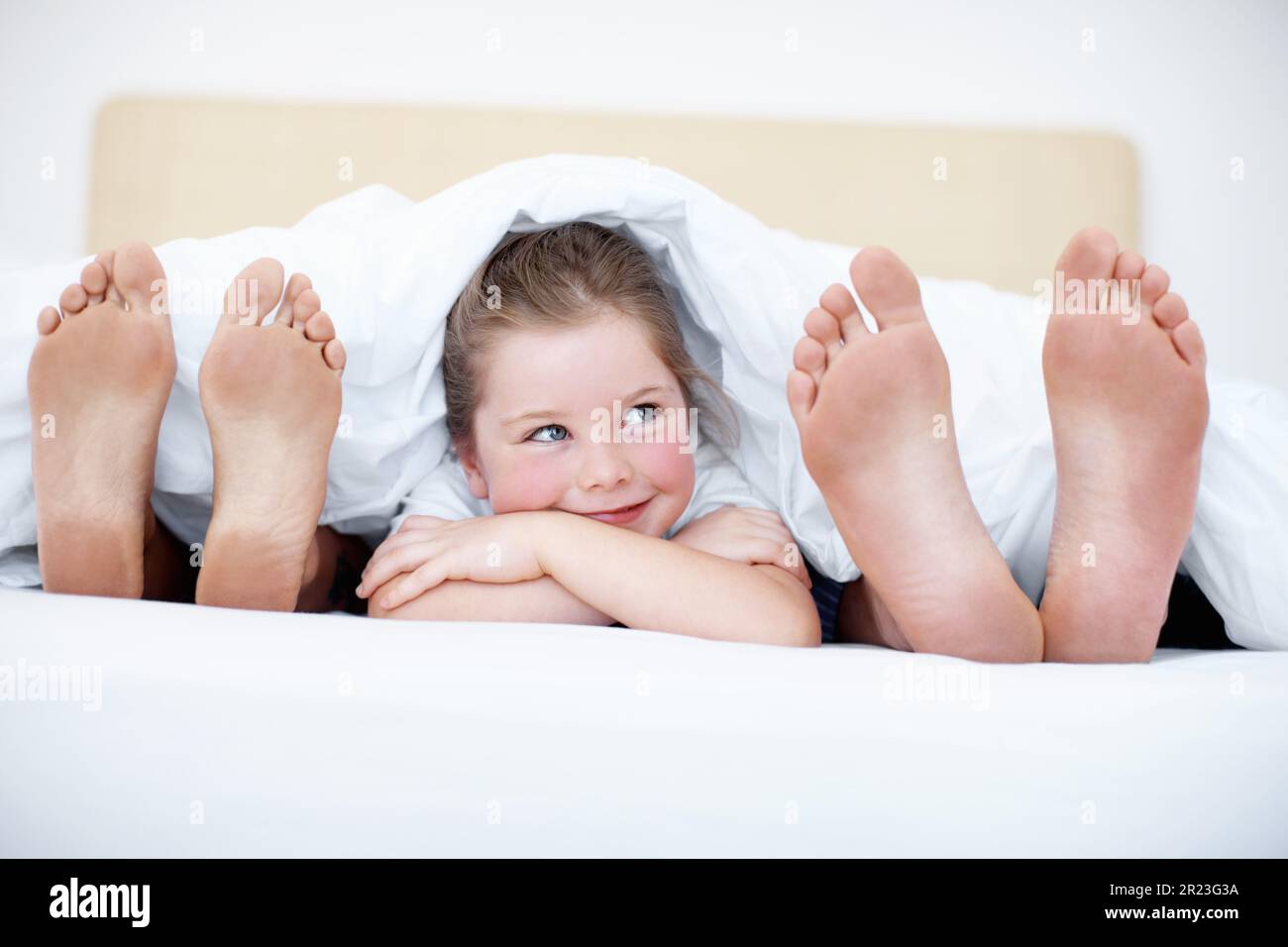 Im about to tickle them sshh..Fun shot of a young girl peeking out from between her parents feet while they lie in bed. Stock Photo