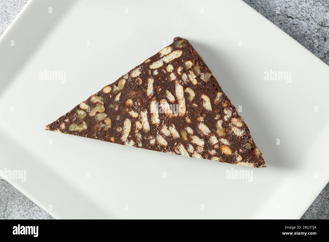 Chocolate mosaic cake with walnuts on a white porcelain plate on a stone background Stock Photo