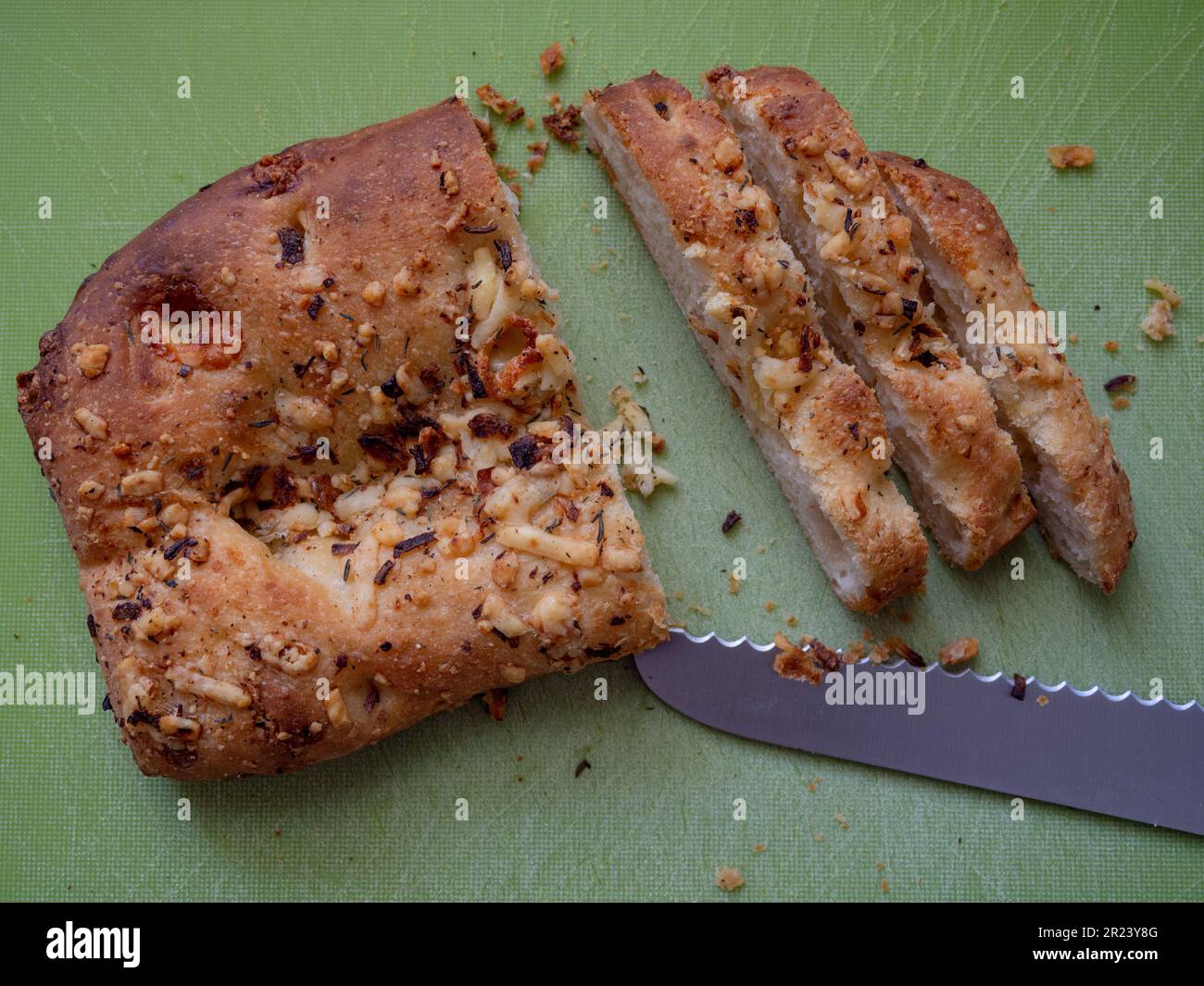 Sliced freshly baked Focaccia bread on a green bread board with a bread knife, UK Stock Photo