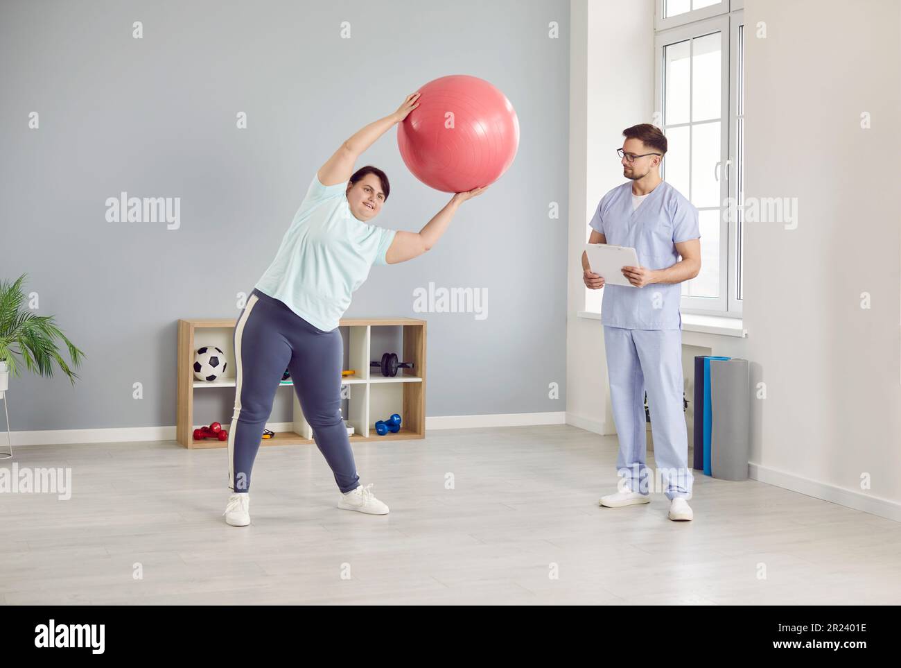 Overweight woman doing exercises with a fit ball under the control of a physiotherapist Stock Photo