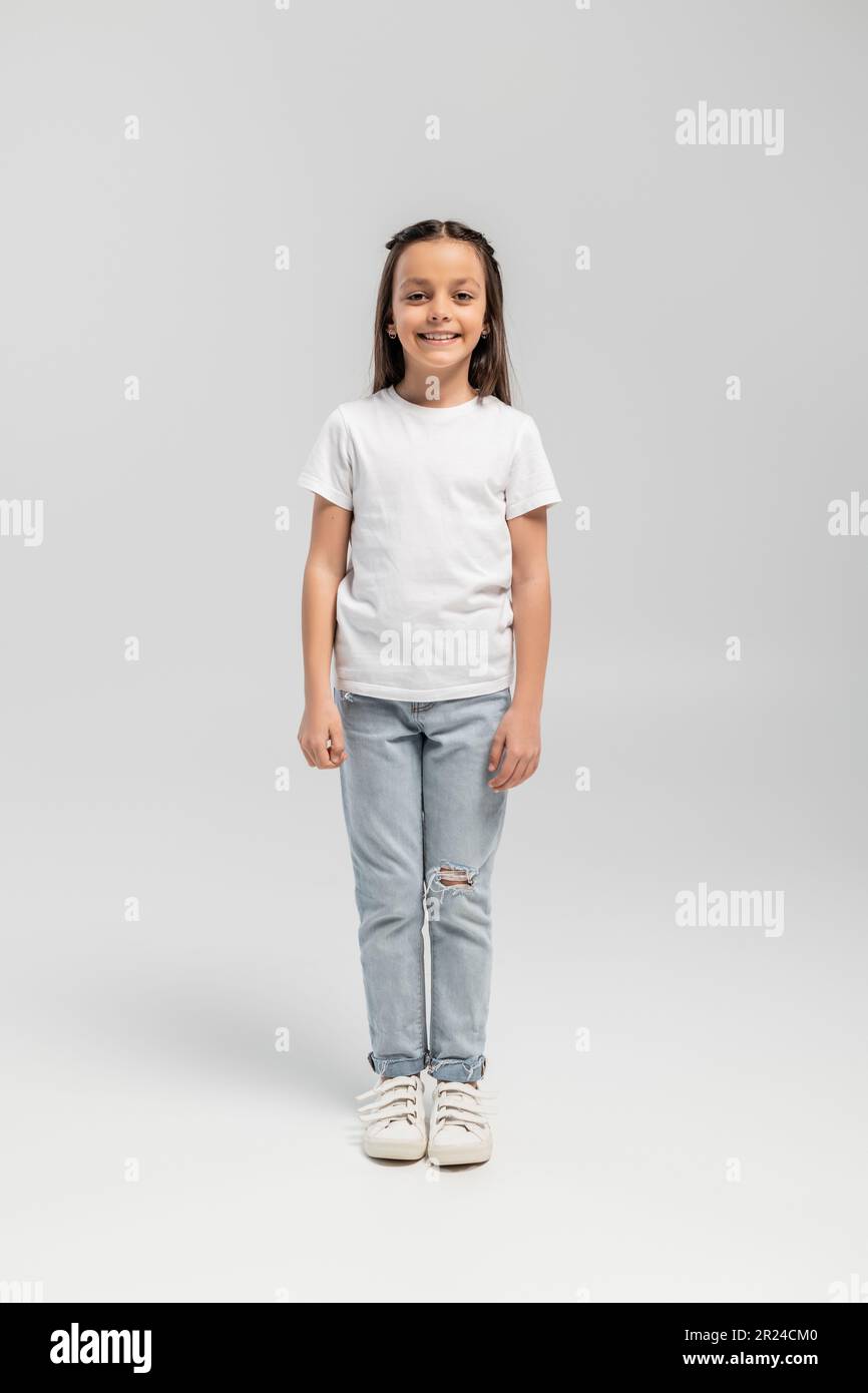 Full length of cheerful and preteen girl in white t-shirt and jeans ...