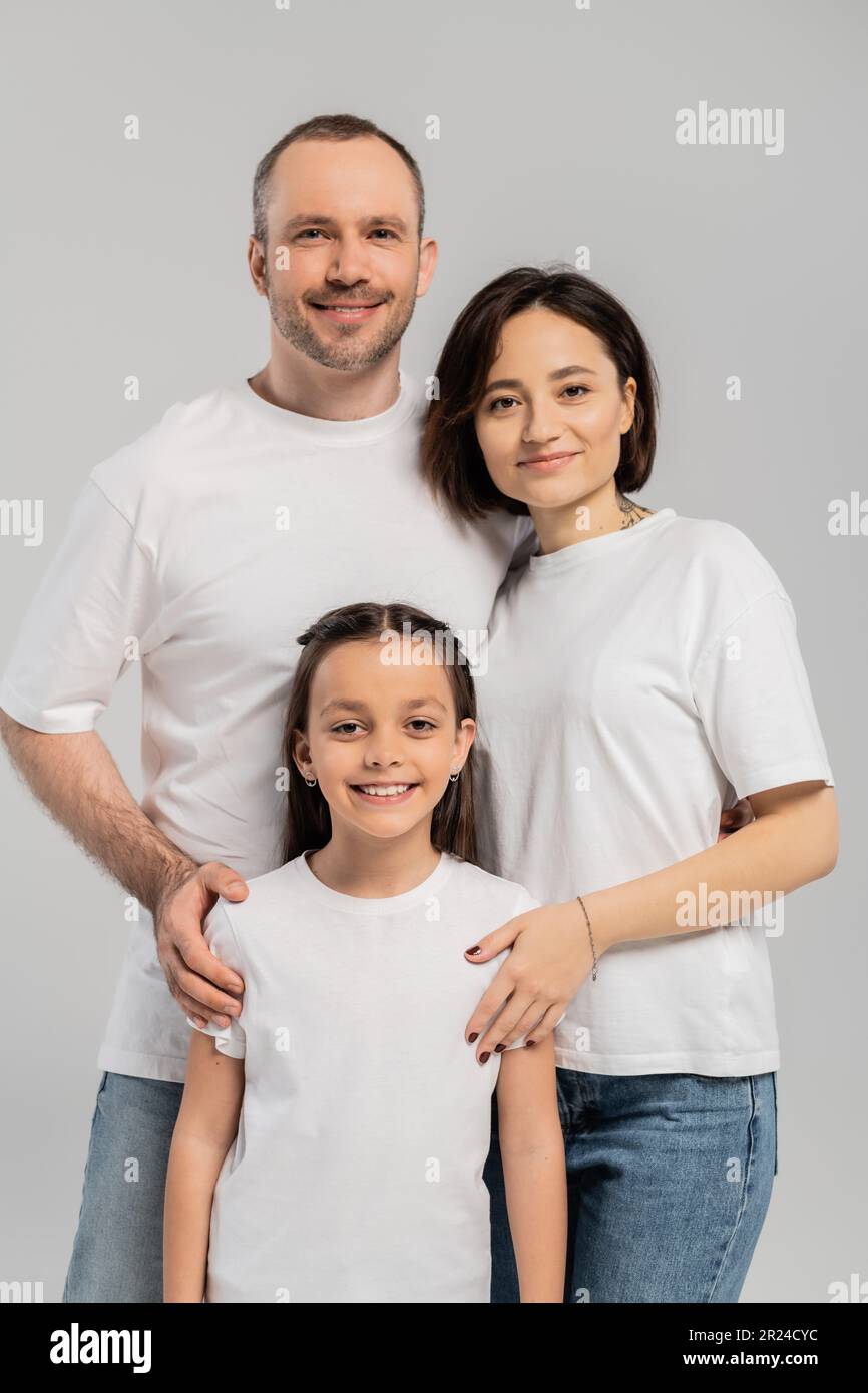 portrait of happy family in white t-shirts looking at camera on grey background, International child protection day, father and mother with tattoo emb Stock Photo