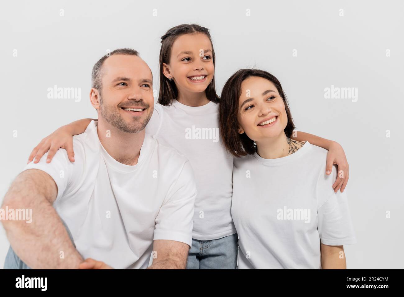 stylish family in white t-shirts looking away while posing together on grey background, International child protection day, preteen daughter hugging h Stock Photo