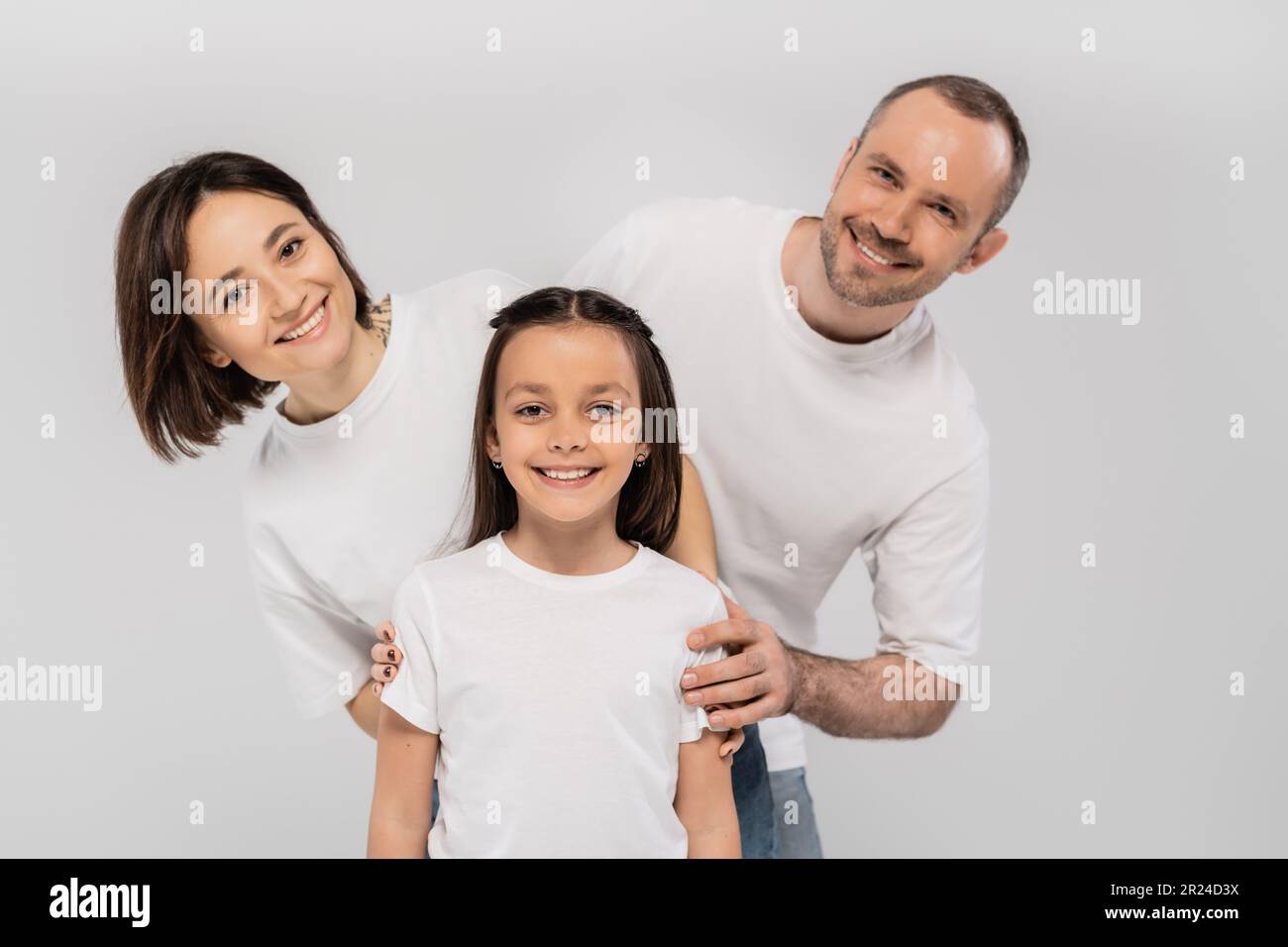 happy family in white t-shirts looking at camera and posing together on grey background, International child protection day, positive father mother an Stock Photo