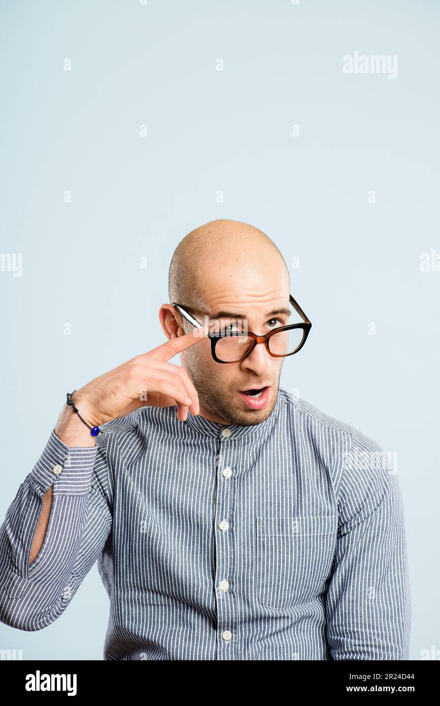 Oh, I see you alright. a handsome young man sitting alone in the studio and pulling funny faces while wearing glasses. Stock Photo