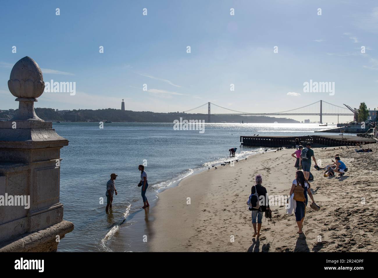 Lisbon, Portugal-October 2022; View of people on city beach on waterfront of historic Praça do Comércio square with view over Tagus river and Ponte 25 Stock Photo