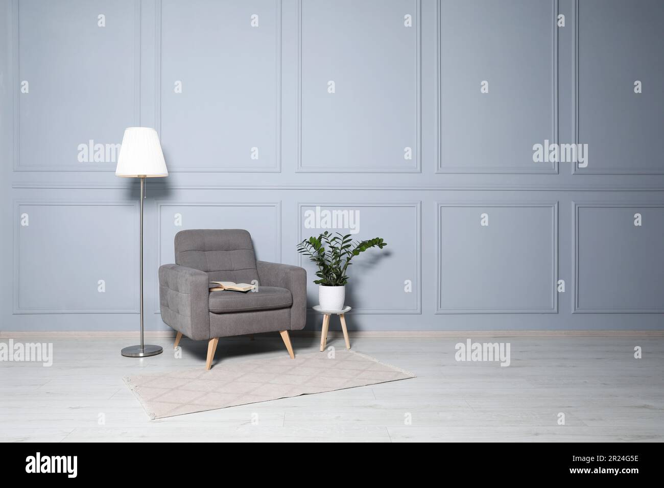 Cosy armchair, floor lamp and potted plant near light grey wall in room ...