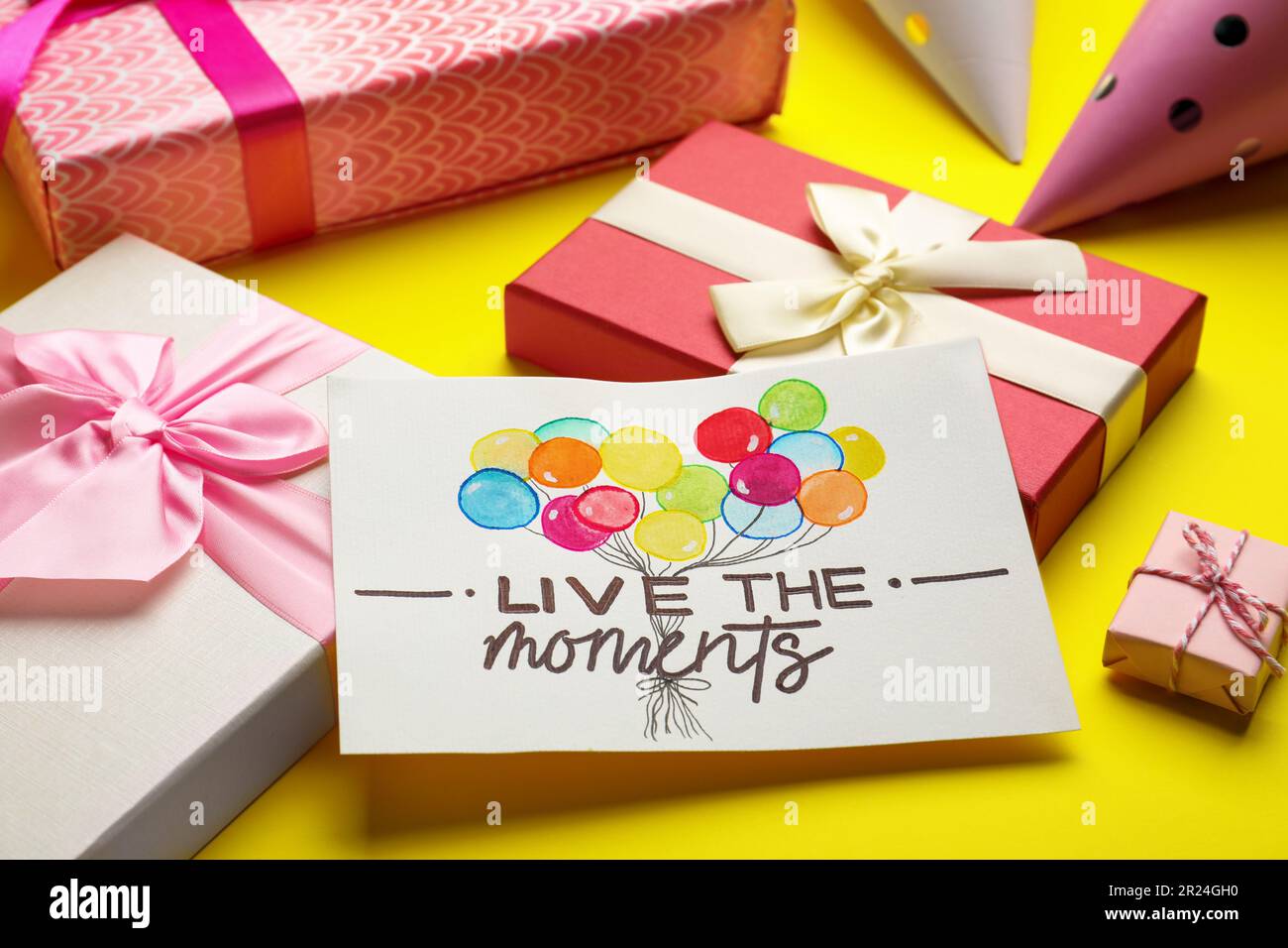 Card with life-affirming phrase Live The Moments and gift boxes on yellow background Stock Photo