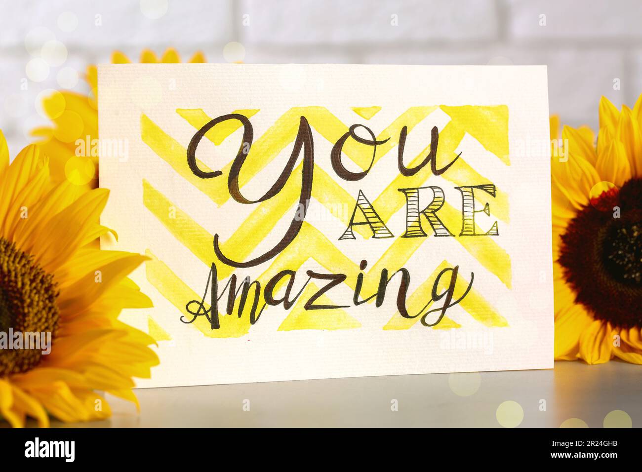 Card with life-affirming phrase You Are Amazing and sunflowers on light table Stock Photo