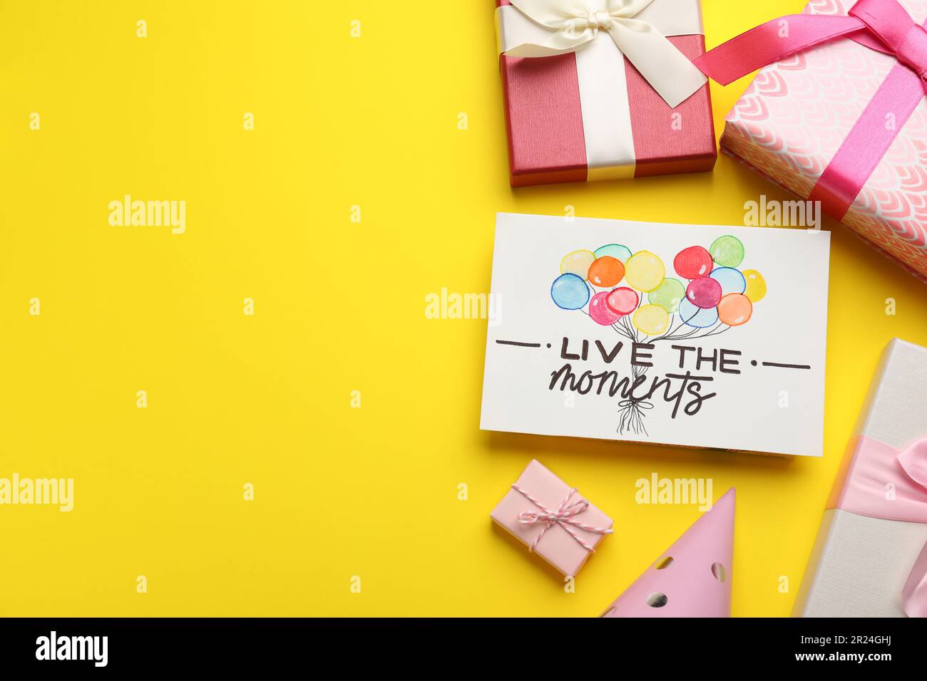 Life-affirming phrase Live The Moments. Flat lay composition with card and gift boxes on yellow background, space for text Stock Photo