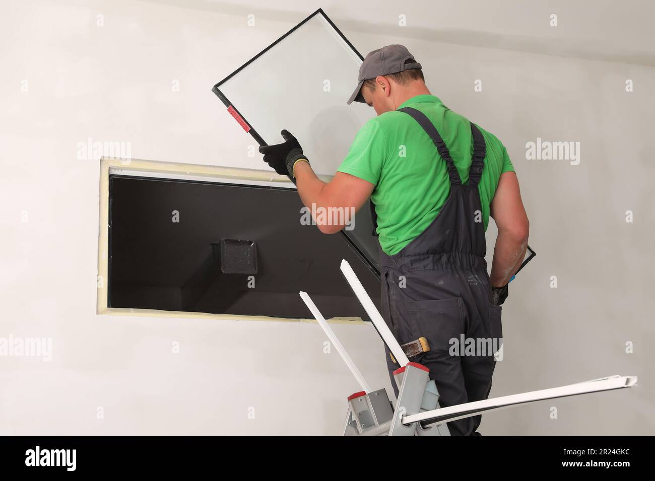 Worker on folding ladder installing window indoors Stock Photo