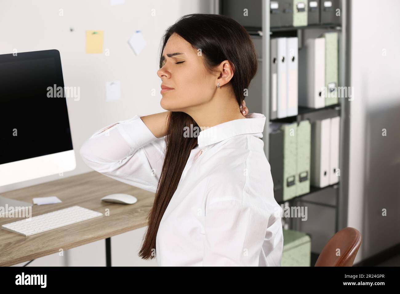 Young woman suffering from neck pain in office Stock Photo - Alamy