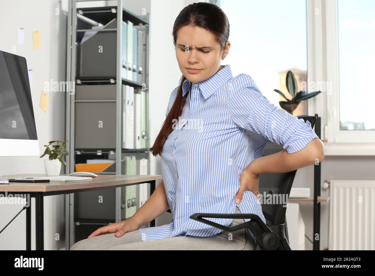 Young woman suffering from back pain while sitting in office. Symptom ...