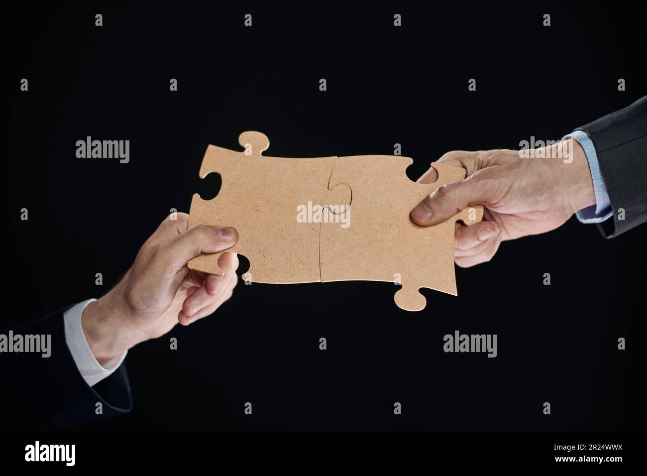 Close-up of business partners putting together white puzzle pieces on black background Stock Photo