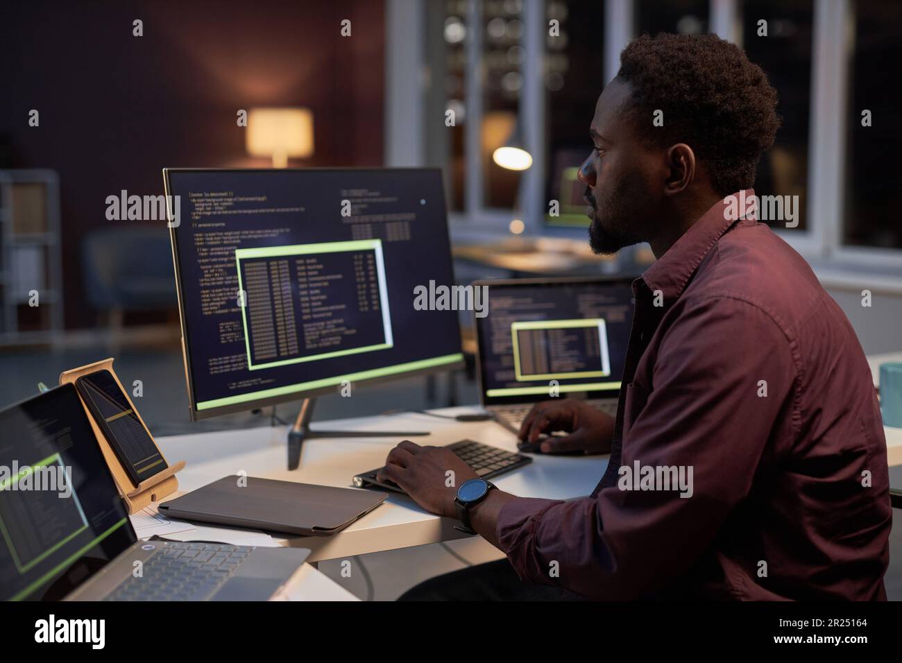 Young African American programmer concentrating on working with codes while sitting at table and working on computer Stock Photo