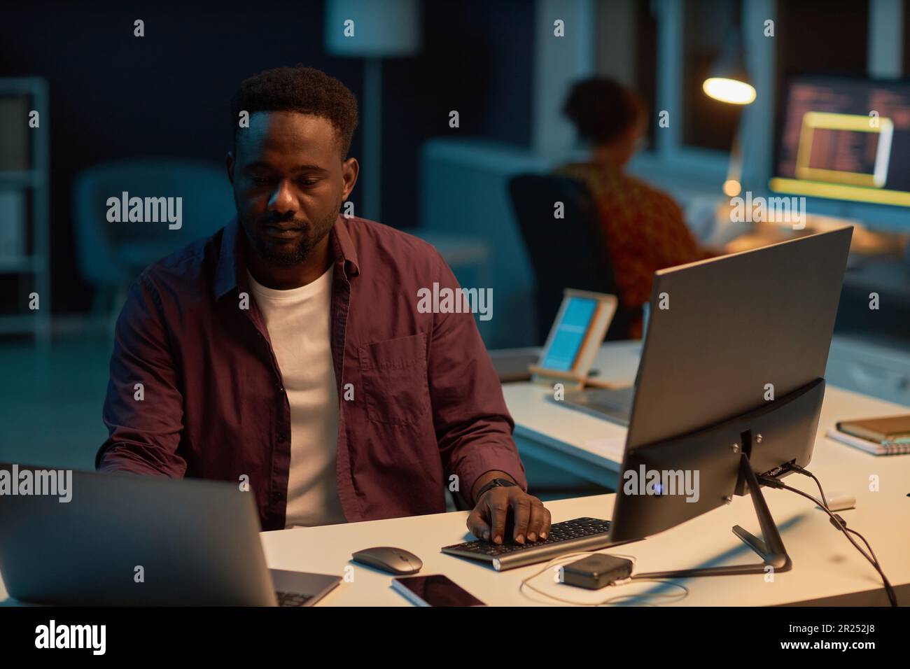 African American developer working on computer at his workplace in dark IT office Stock Photo