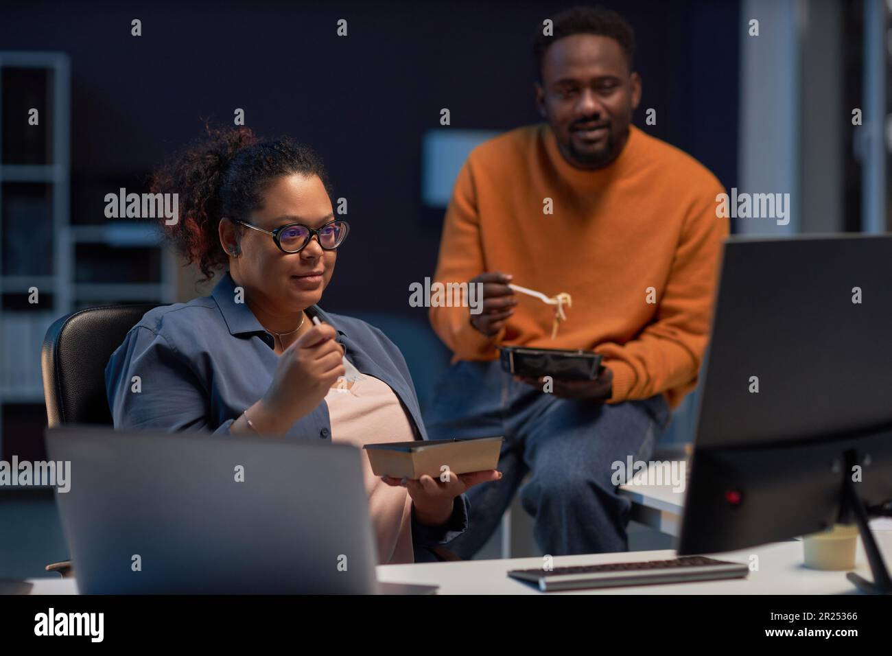 Programmers having lunch while discussing computer program on computer in dark office Stock Photo