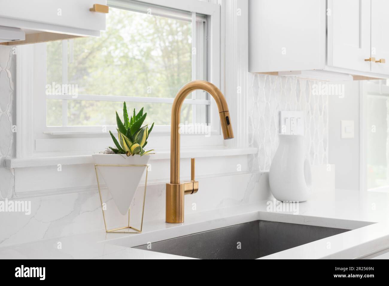 A kitchen sink detail with a gold faucet, marble tile backsplash, and