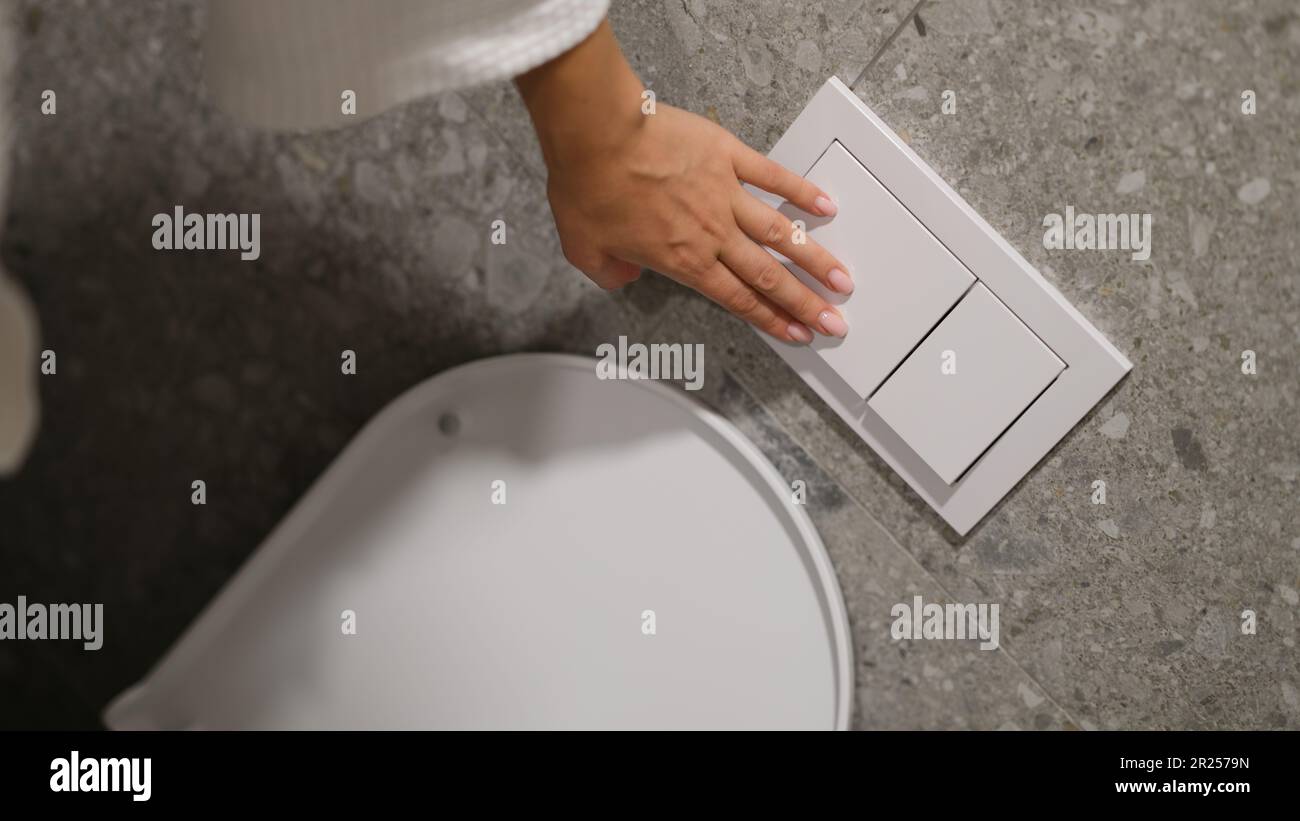 Hand pressing button to drain water in toilet bowl in restroom closeup