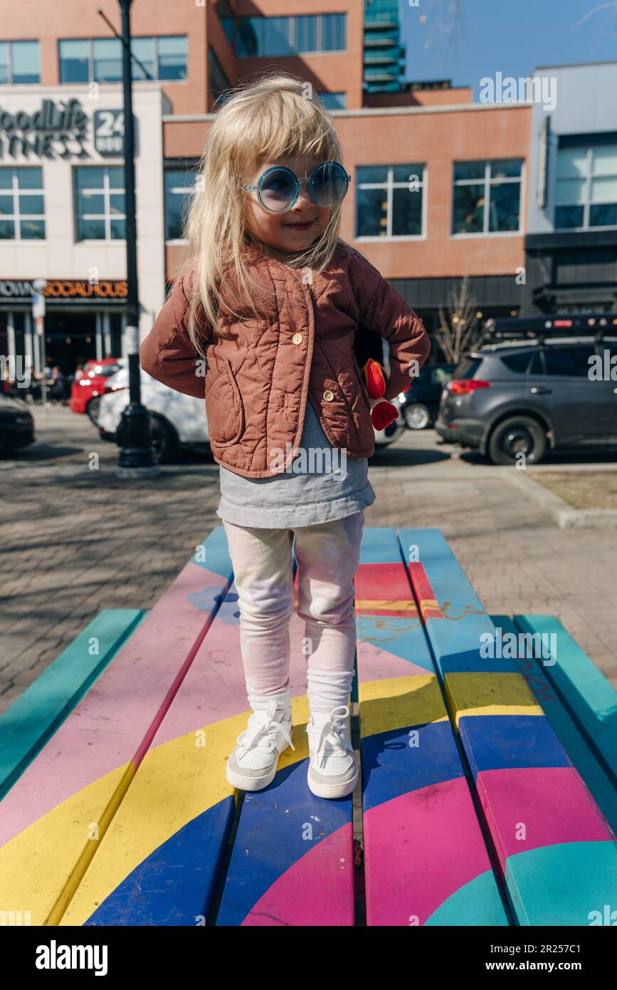 a little girl in blue glasses sits on a multi-colored bench. High ...