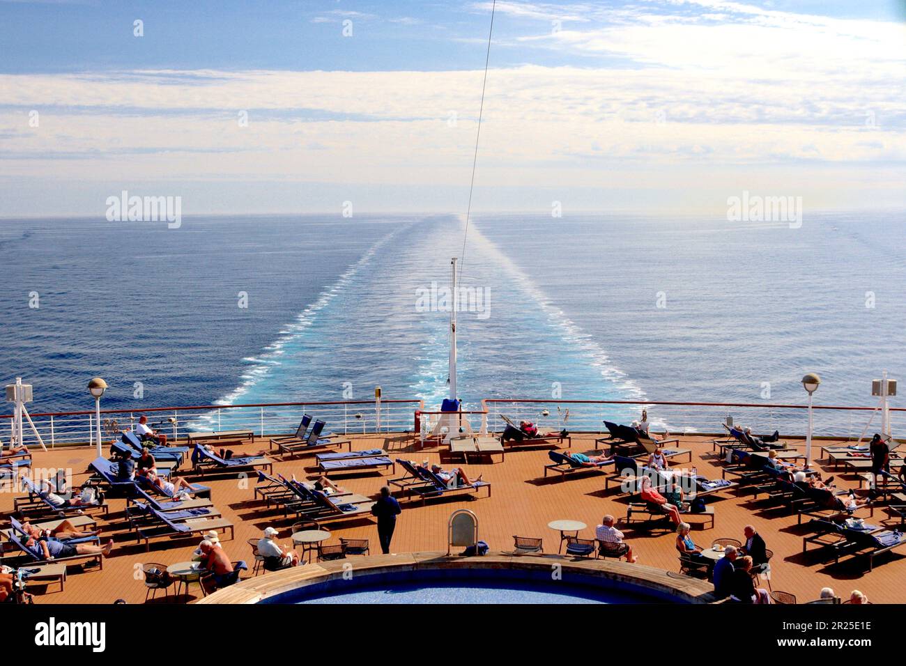 Populated sunbeds appear magnetically aligned to the afternoon sun surrounding the Aquarius pool situated at the stern of the P&O cruise ship Arcadia. Stock Photo