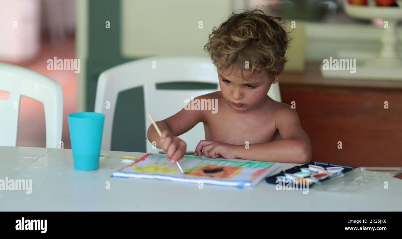 Young boy painting at home. Child crafting using aquarelle paint, kid doing artistic homework drawing Stock Photo