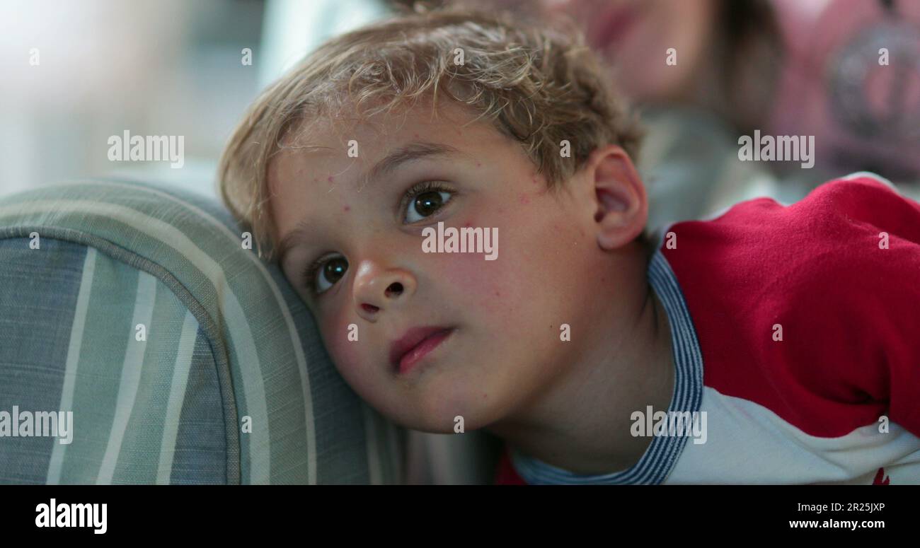 Toddler child staring at TV screen hypnotized. Boy watching screen on sofa before bed Stock
