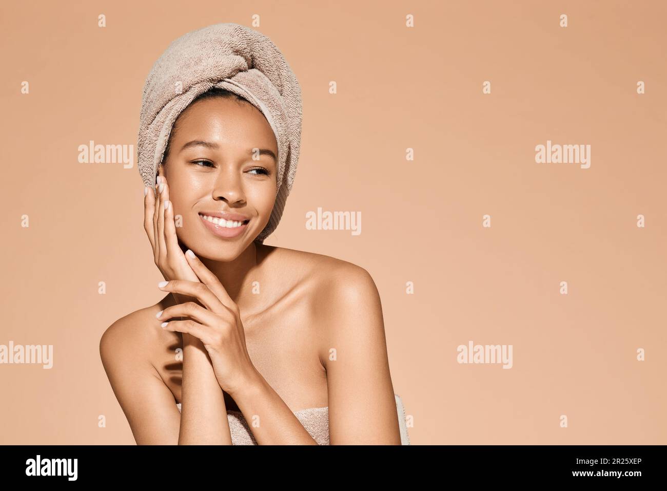 beauty portrait of African woman with perfect skin and towel around her head on beige background. Body care concept Stock Photo