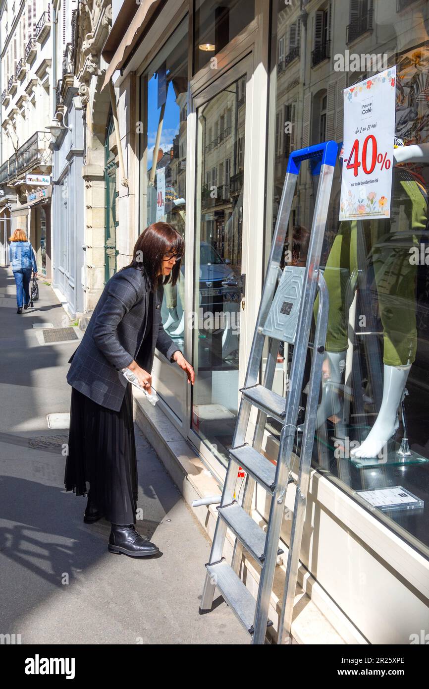 Elegantly dressed woman cleaning shop window - Tours, Indre-et-Loire (37), France. Stock Photo