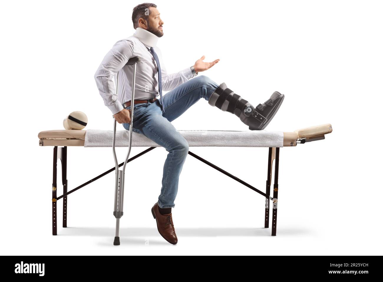 Injured man with an orthopedic boot and neck collar sitting on a therapy table and gesturing with hand isolated on white background Stock Photo