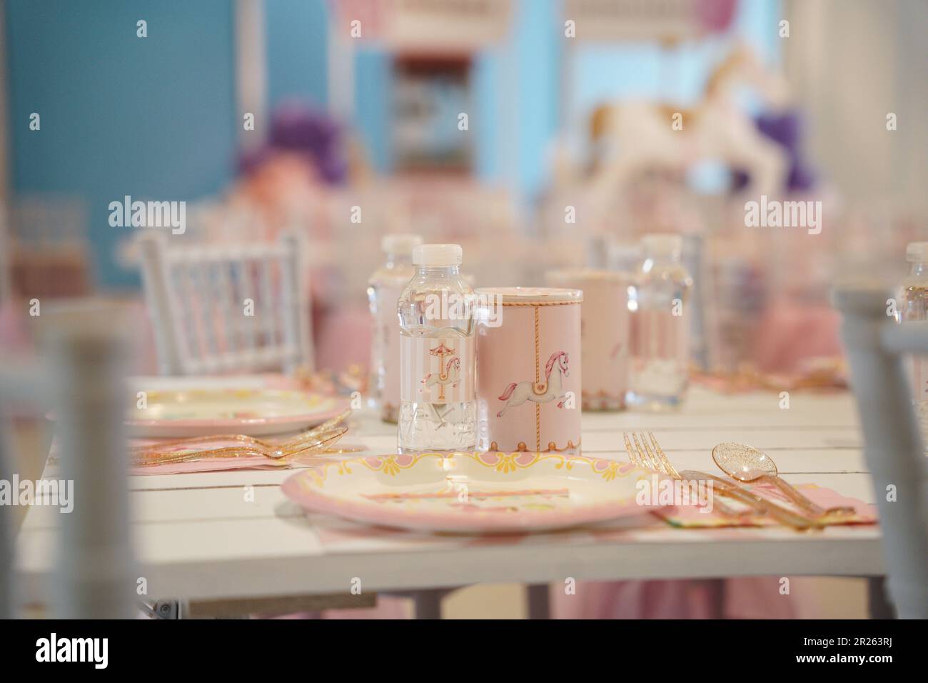 Kid's horse carousel or carnival-themed party table with plastic plates and candy. Festive decoration for a little girl's birthday party with lunch ta Stock Photo