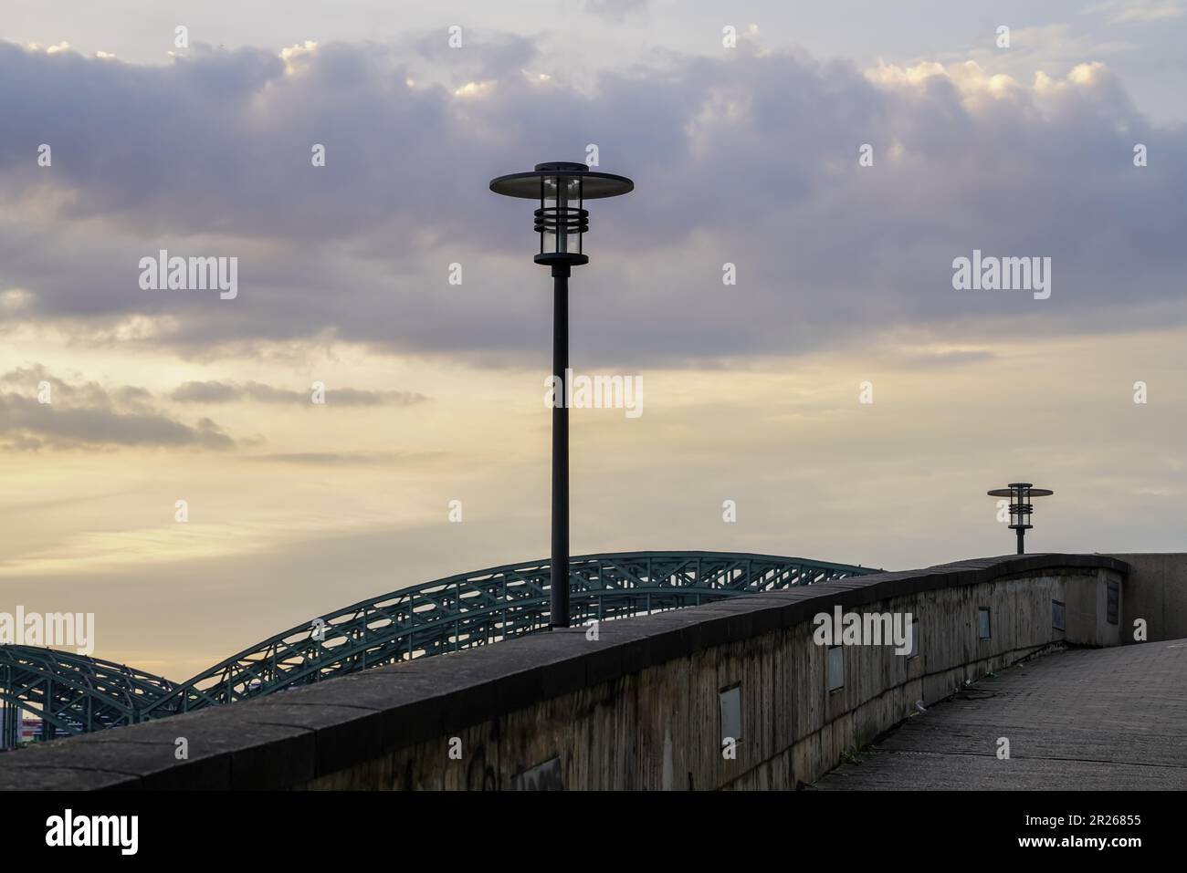 View in the early evening hours from a footpath to two streetlights that are not yet lit. Stock Photo