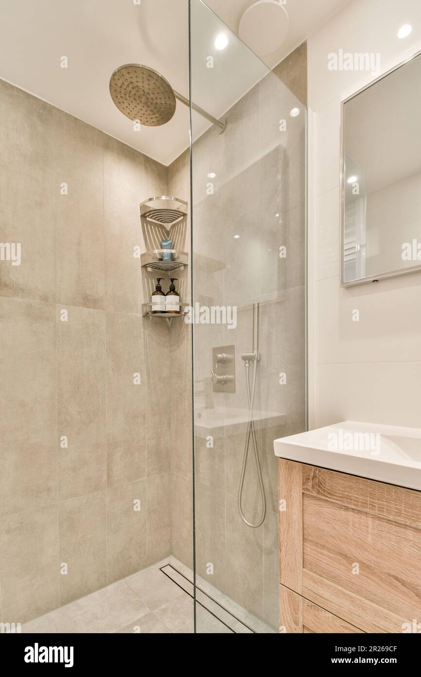 a bathroom with a glass shower door and wooden vanity in the corner next to  the walk - in shower stall Stock Photo - Alamy