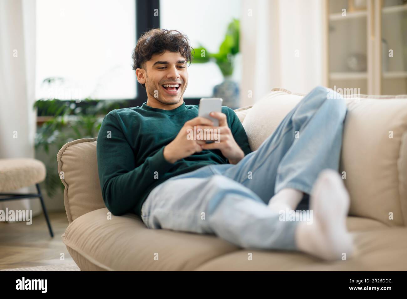 Happy Middle Eastern Young Man Using Cellphone Laughing At Home Stock Photo