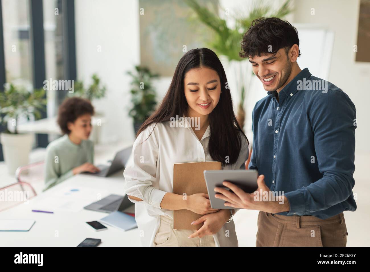 Two Colleagues Using Tablet Discussing Ideas In Office, Enjoying Teamwork Stock Photo