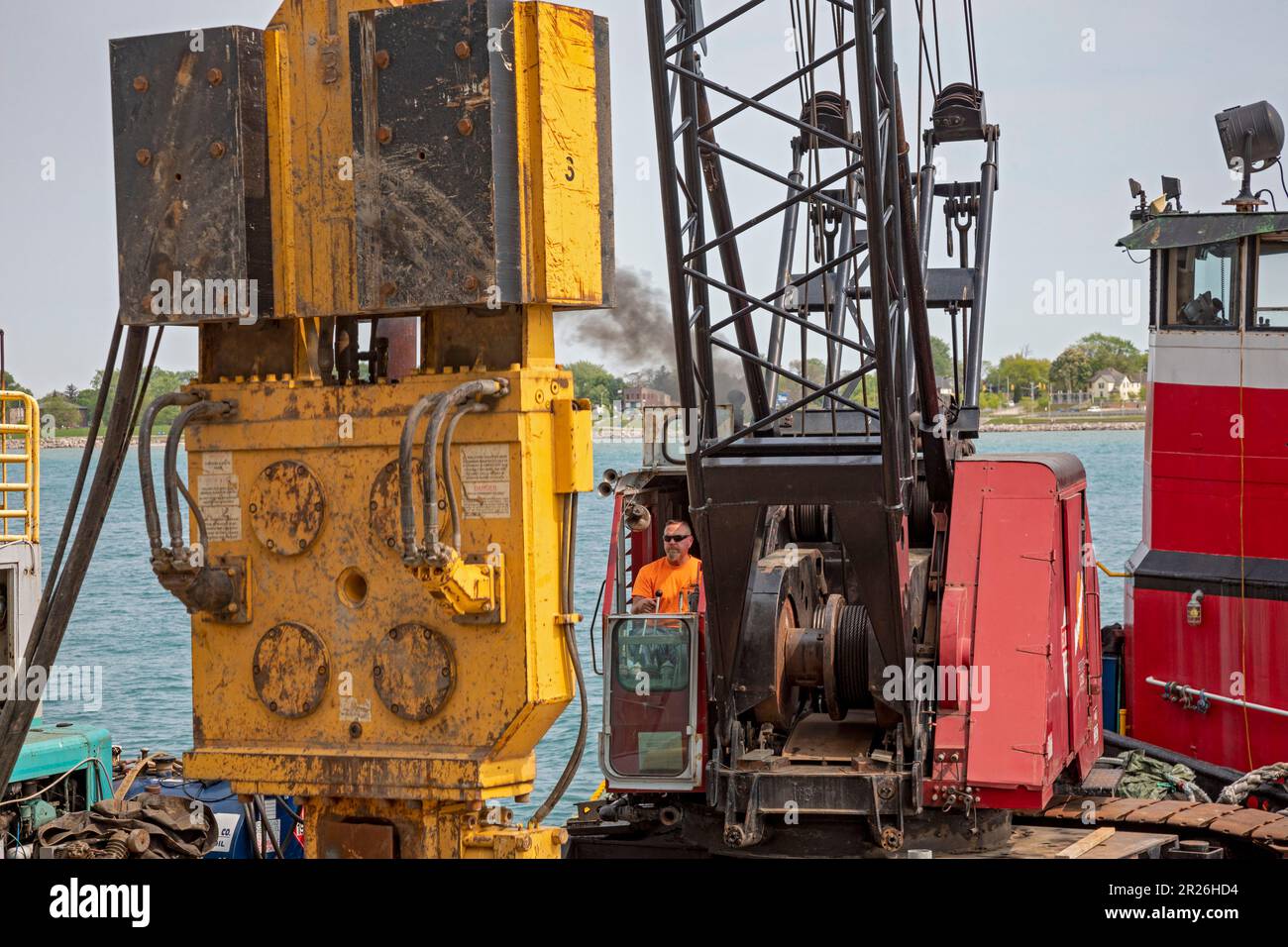 Detroit, Michigan - Workers repair the seawall along the Detroit Riverwalk using a pile driver mounted on a barge on the Detroit River. Stock Photo