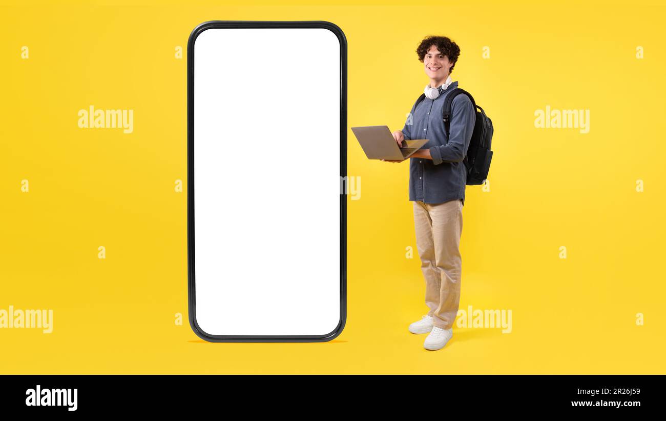 Student Using Laptop Posing With Huge Phone On Yellow Background Stock Photo
