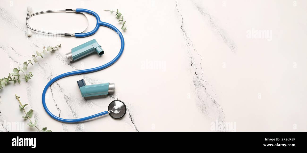 Asthma inhalers, stethoscope and eucalyptus branches on light