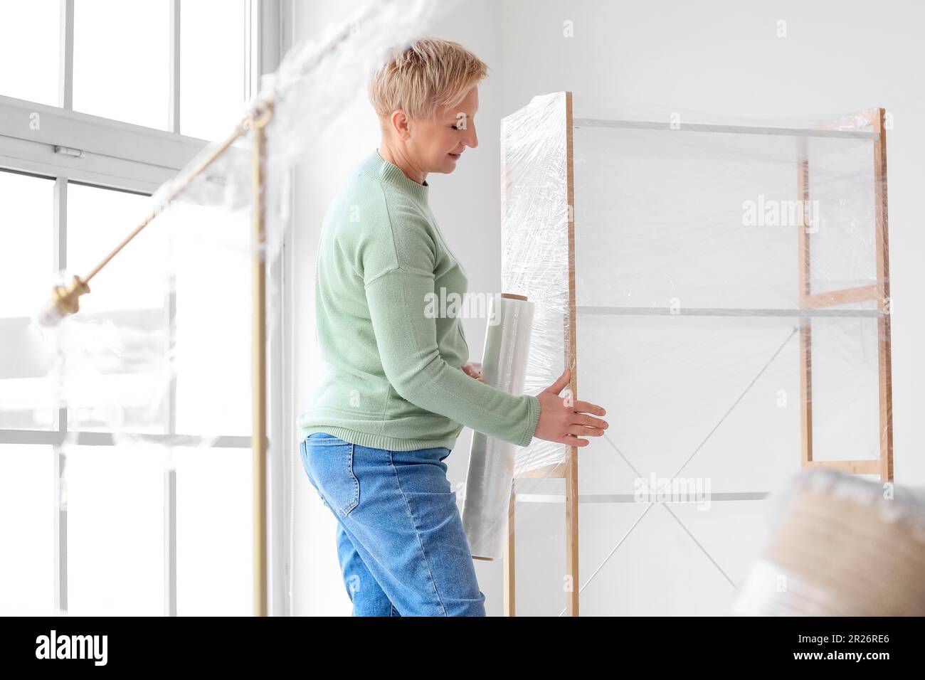 Mature woman wrapping shelving unit with stretch film at home Stock Photo