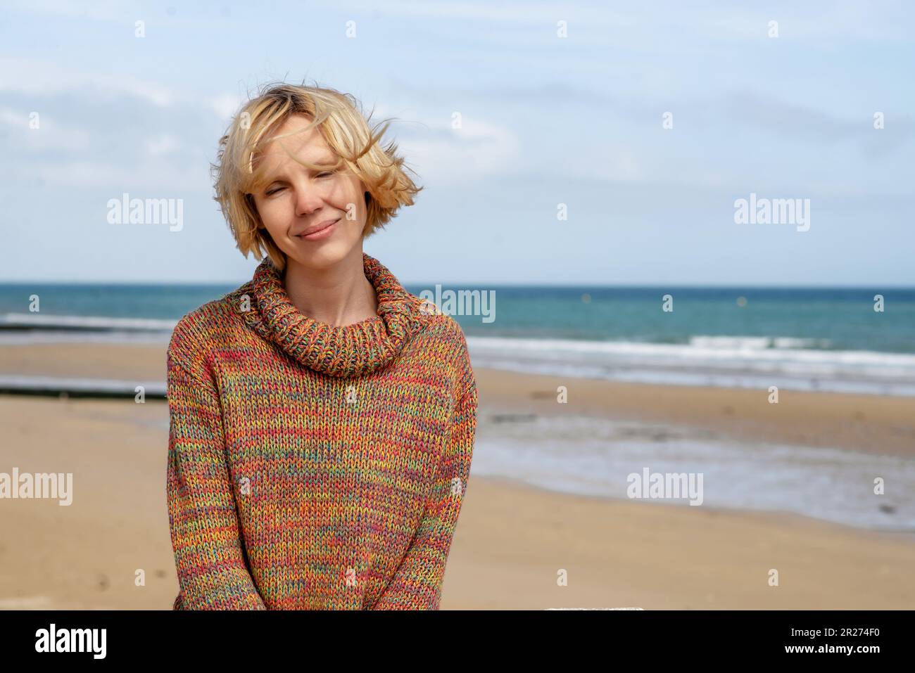 Woman in a sweater on the ocean, sea. Attractive middle-aged woman with windblown hair smiling. Sunny weather, rest, relaxation on vacation. Place for Stock Photo