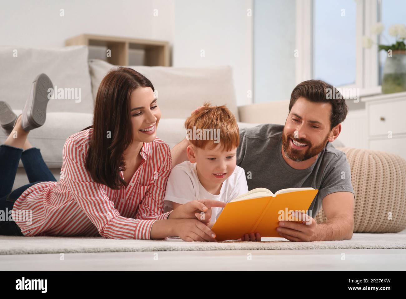 Happy parents with their child reading book on floor at home Stock ...