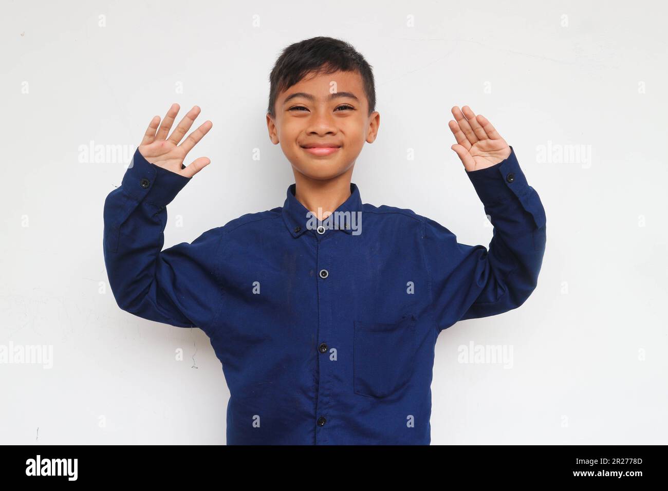 Cheerful little boy in express smiling face while raised the hands, isolated on white background. A 10 years old boy making a funny face. Stock Photo