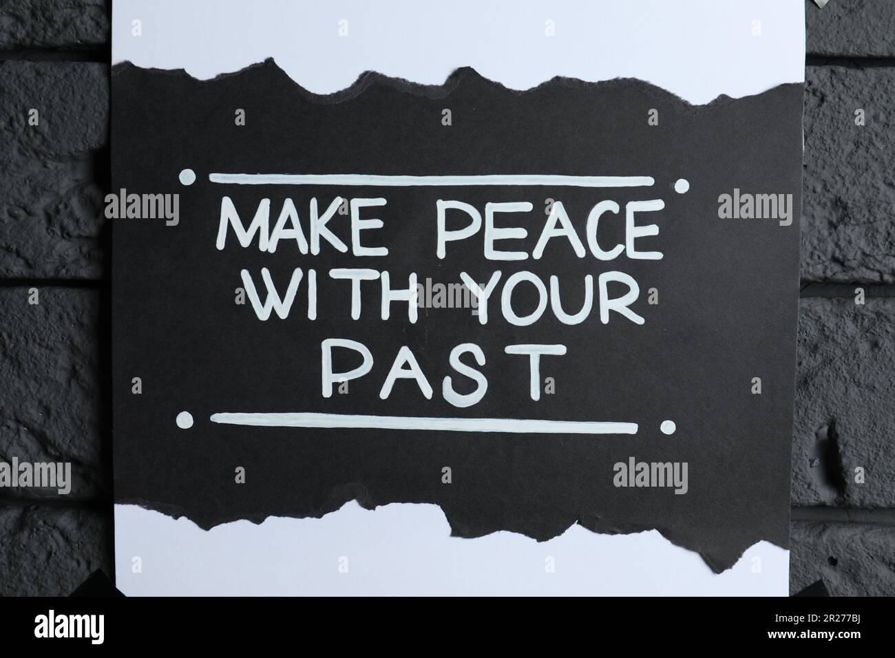 Card with life-affirming phrase Make Peace With Your Past on dark brick wall, closeup Stock Photo