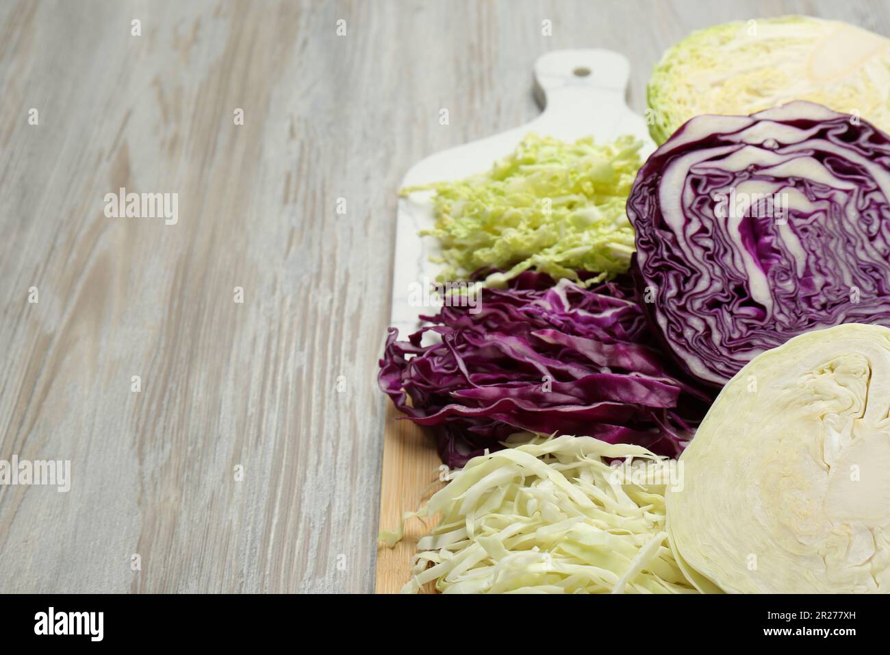 Different types of cut cabbage on white wooden table, space for text ...