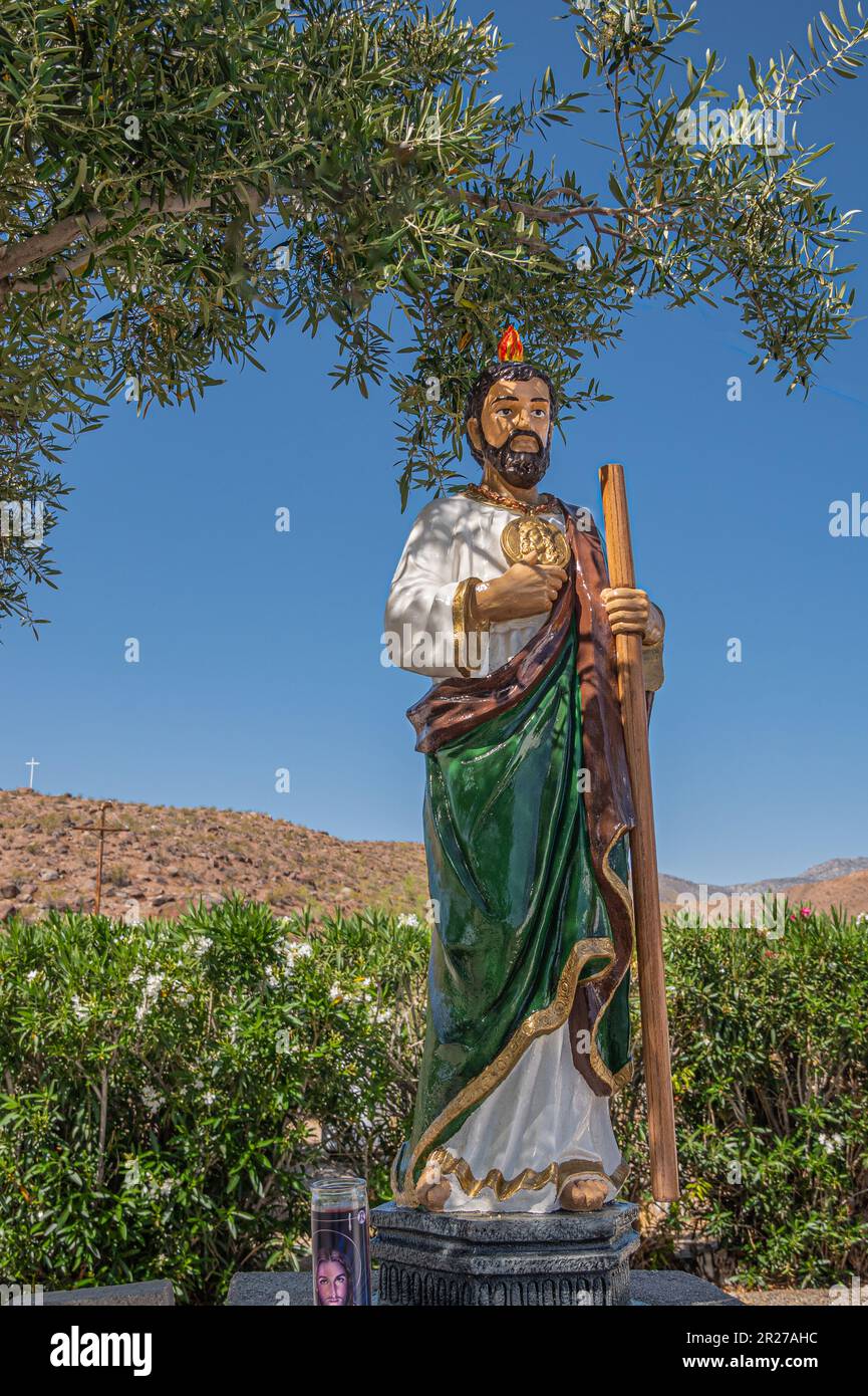 Borrego Springs, CA, USA - April 24, 2023: St. Jude Thaddeus colorful statue at Saint Richards Church against blue sky, surrounded by green foliage. S Stock Photo