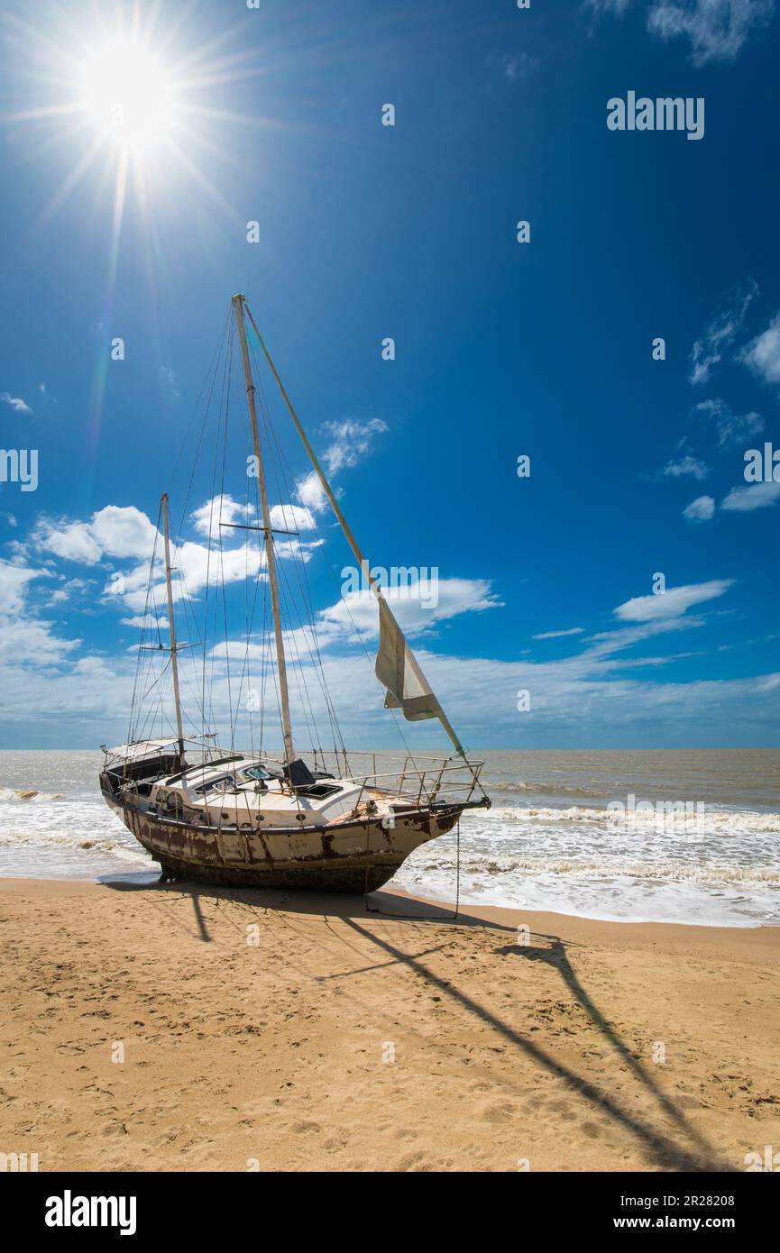 Having broken its mooring during stormy weather an old abandoned sailing Yacht lays stranded at Yorkeys Knob Beach in Cairns, Queensland in Australia. Stock Photo